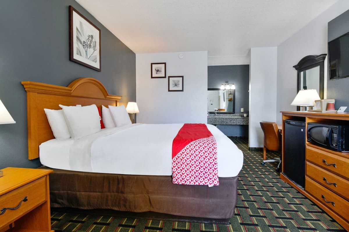 A hotel room with a large bed, a desk with a computer, a microwave, and a small refrigerator.