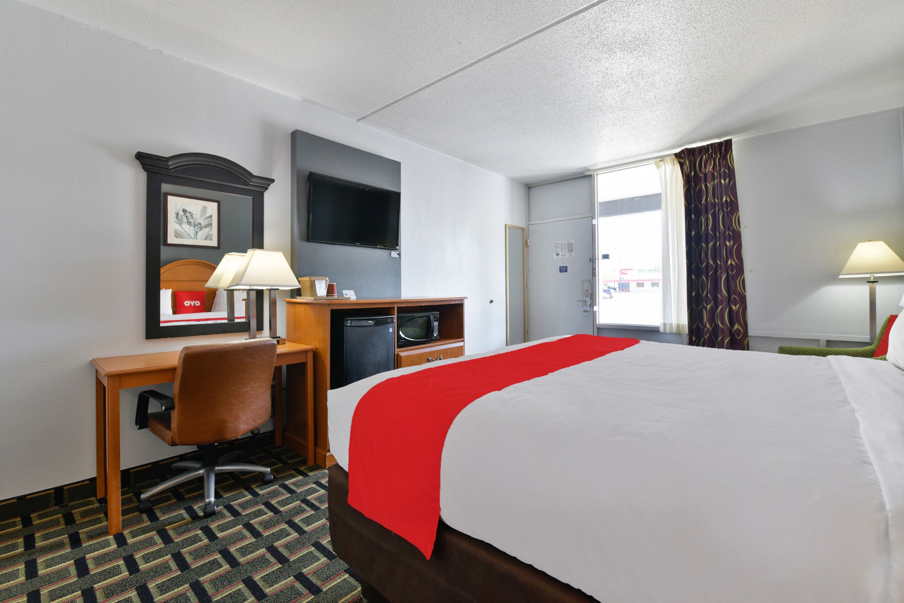 Een hotelkamer met een bed, bureau, stoel, televisie en een raam met gordijnen.
