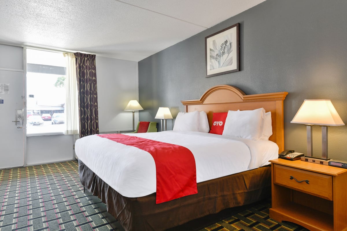 A hotel room with a large bed, two bedside lamps, a bedside table with a phone, and a window with curtains.