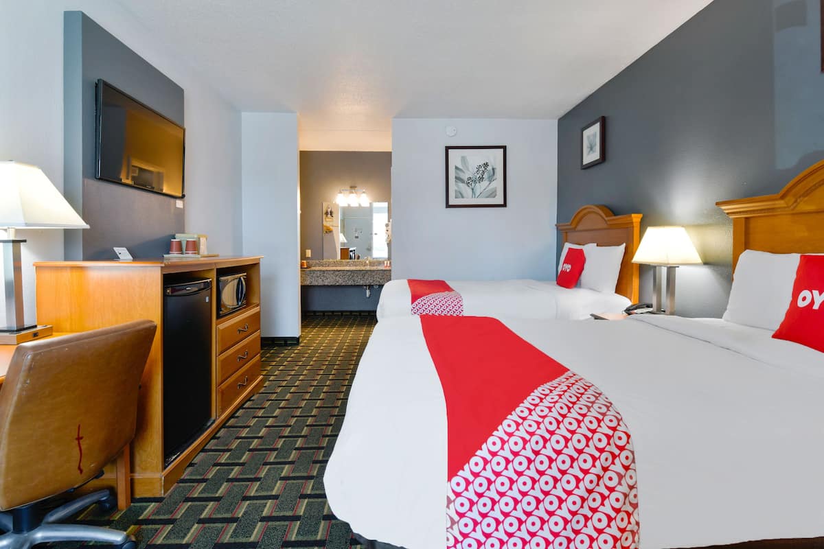 A hotel room with a bed, desk, and a view of the hallway.