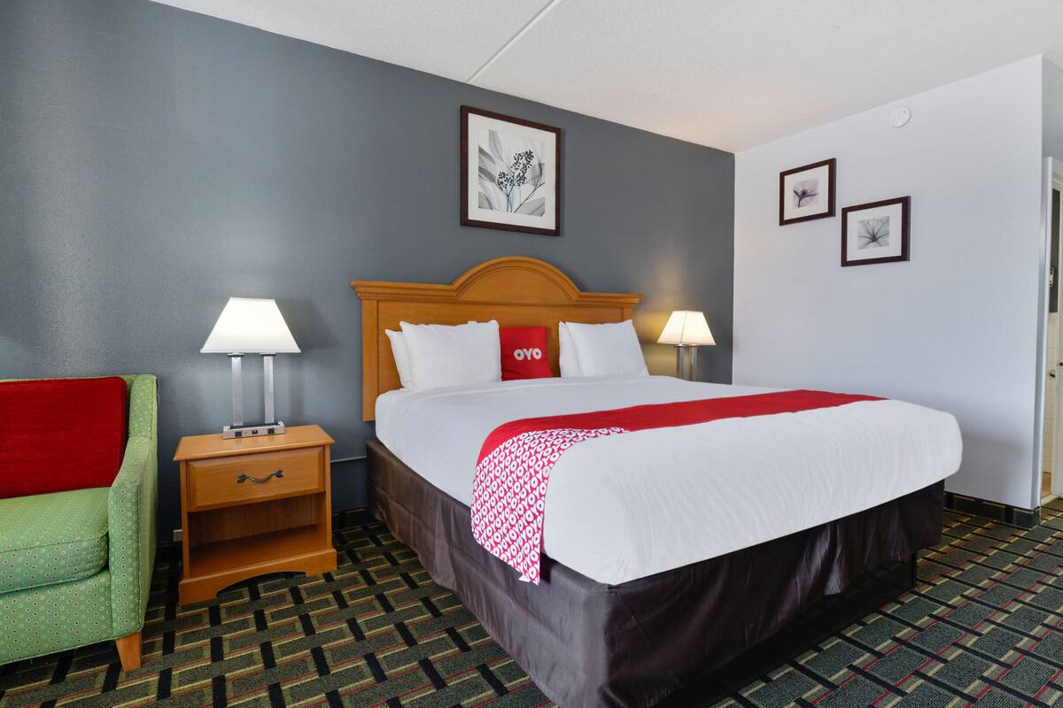 A hotel room with a large bed, two bedside tables with lamps, a green armchair, and a patterned carpet.