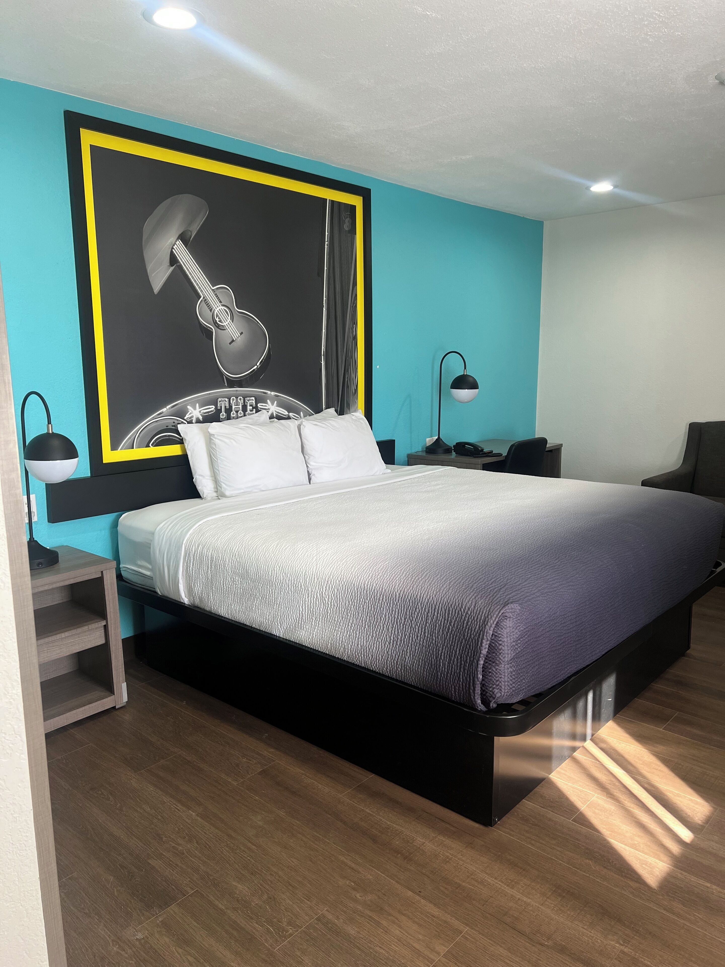 Une chambre moderne avec un lit, des tables de chevet, une lampe et une affiche de guitare au mur.