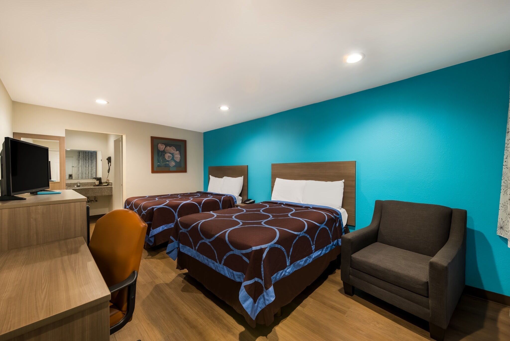 A hotel room with two beds, a desk, a chair, and a television.