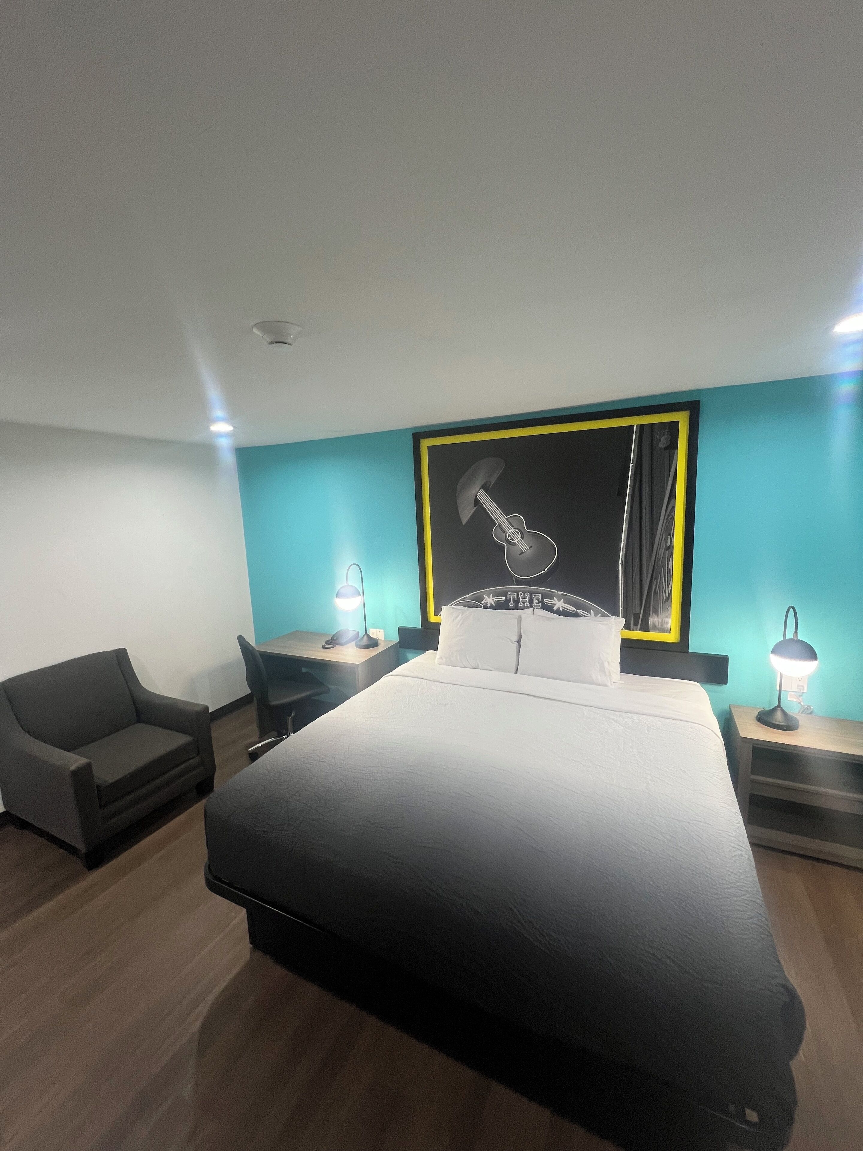 A hotel room with a large bed, a desk, a chair, and a wall-mounted artwork.