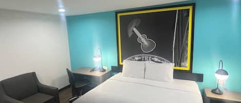 A hotel room with a large bed, a desk, a chair, and a wall-mounted artwork.