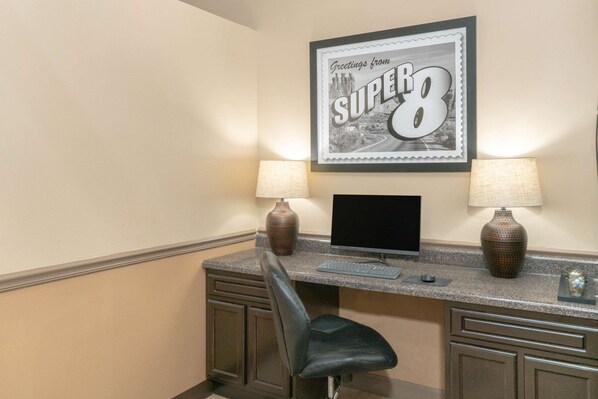 A hotel room with a desk, two lamps, a computer, and a framed picture on the wall.
