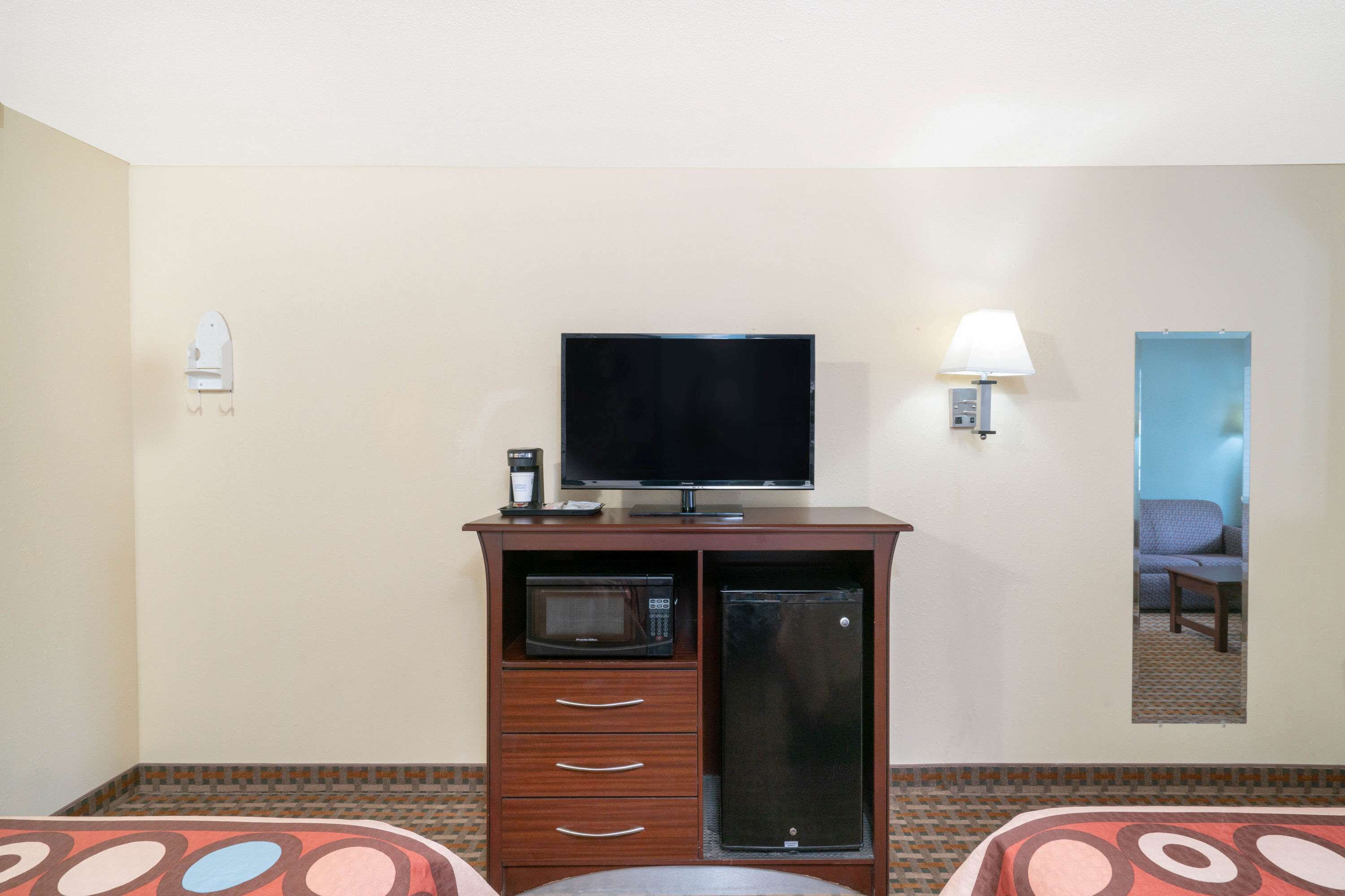 A hotel room with a TV, microwave, refrigerator, and a lamp.