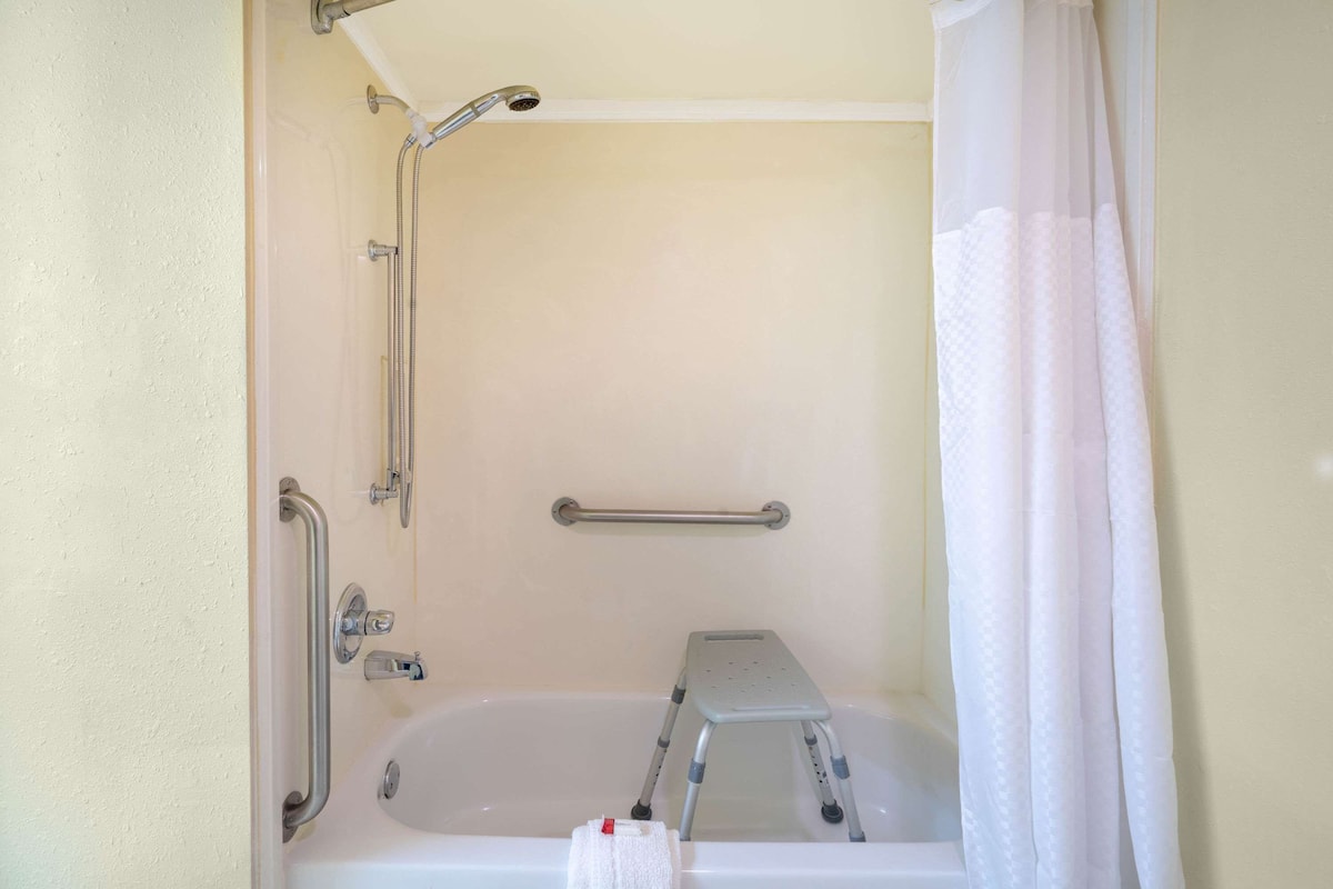 A bathroom with a bathtub, shower, grab bars, and a step stool.