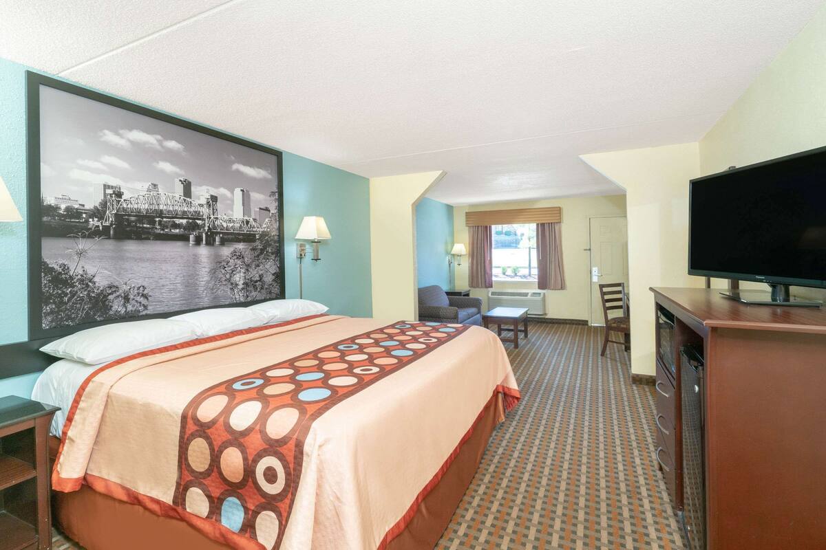 A hotel room with a bed, a desk, a television, and a large window.