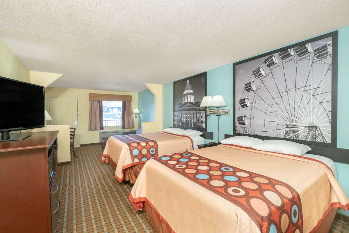 A hotel room with two beds, a TV, a desk, and a large wall mural.