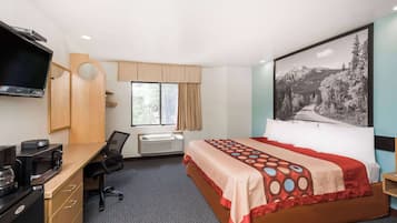 A hotel room with a bed, a desk with a computer, a TV, and a window with curtains.