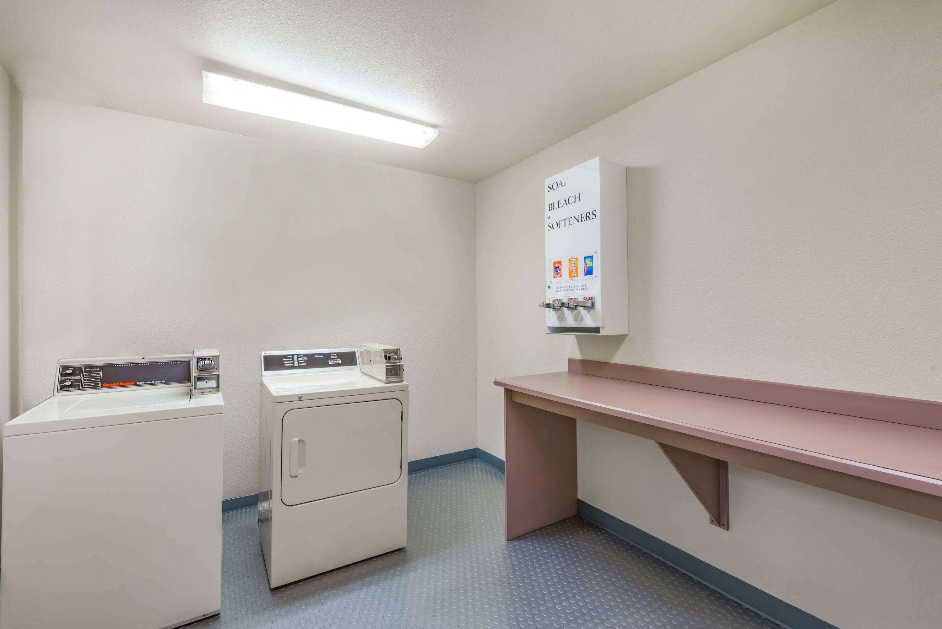 Une buanderie équipée de deux machines à laver, d’un évier et d’un tableau d’affichage où sont accrochés des produits de lessive.