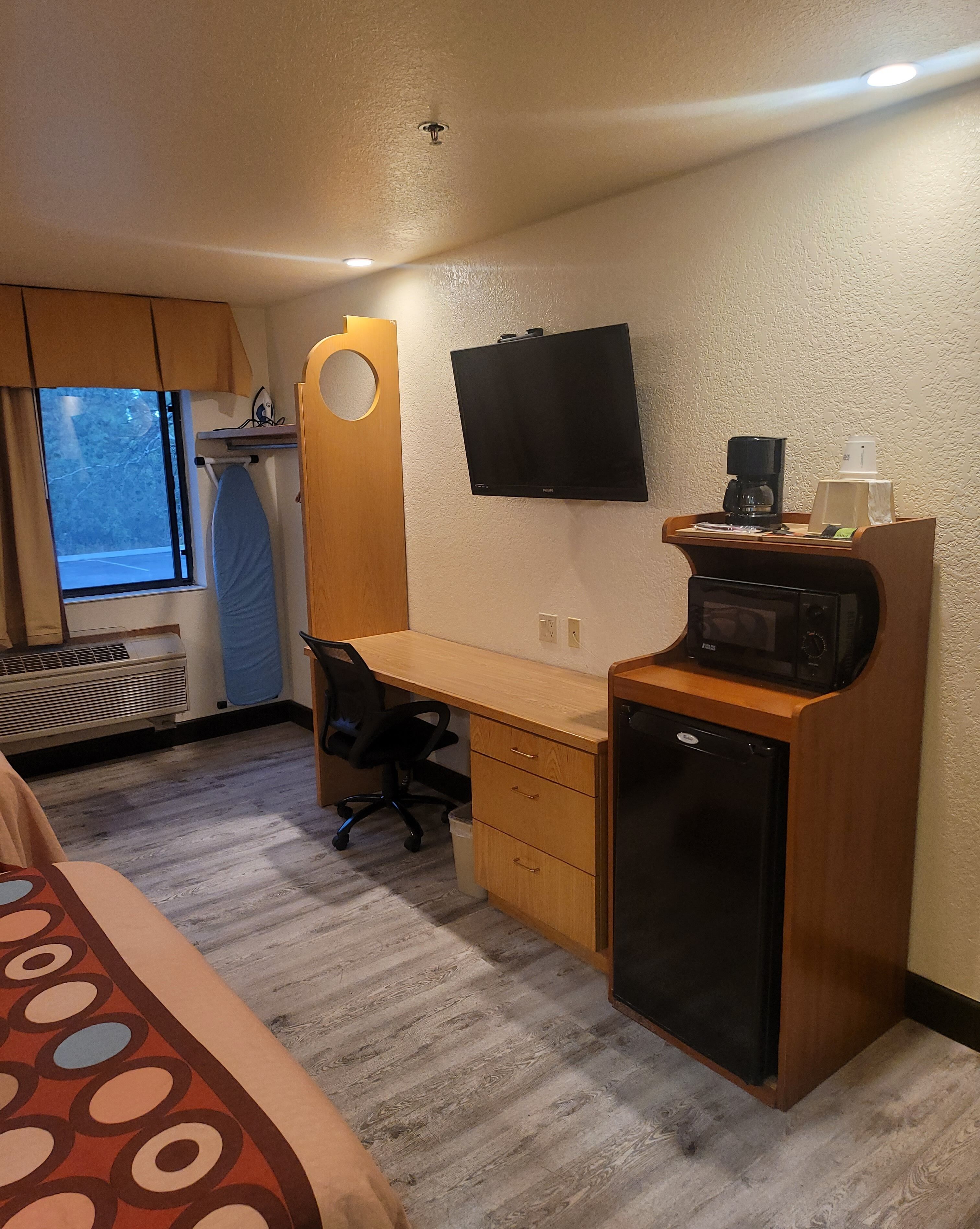 Une chambre d’hôtel de taille réduite, comprenant un lit, un bureau avec une chaise, un four à micro-ondes, une télévision et une fenêtre avec des rideaux.