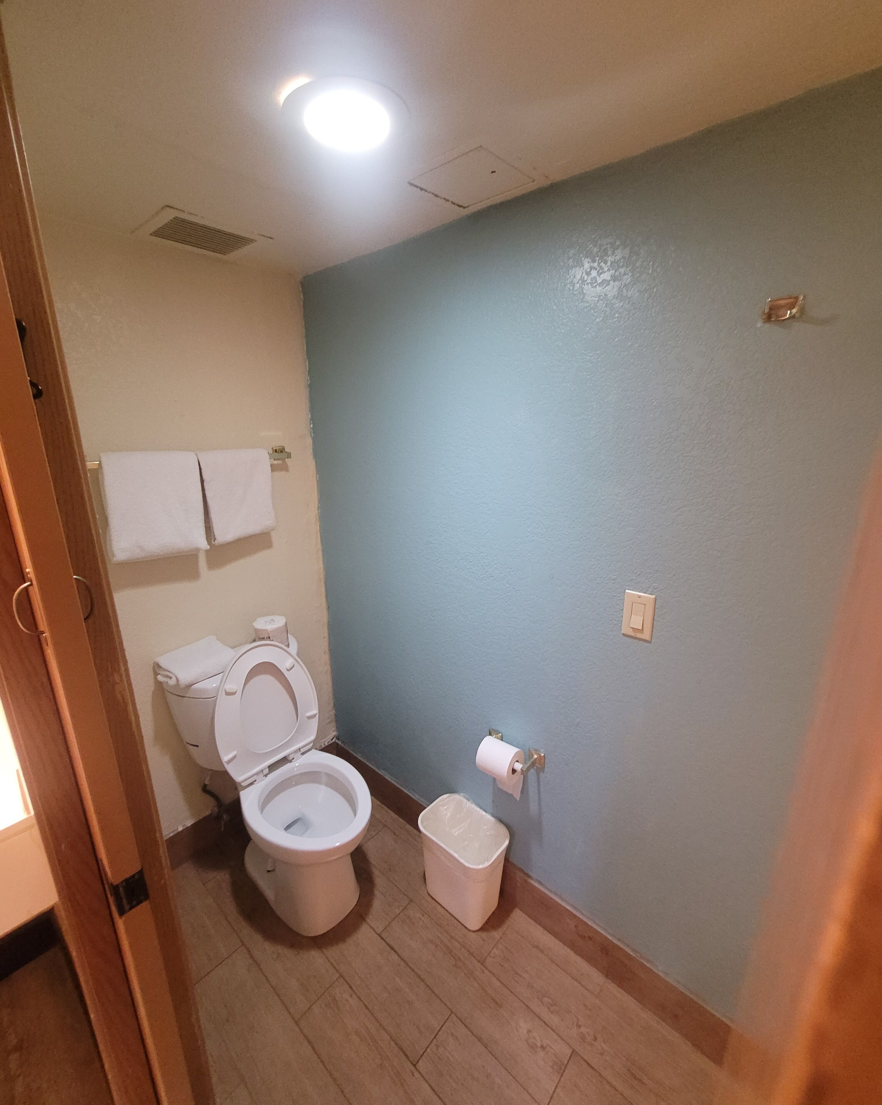 A small bathroom with a toilet, a trash bin, and a towel rack.