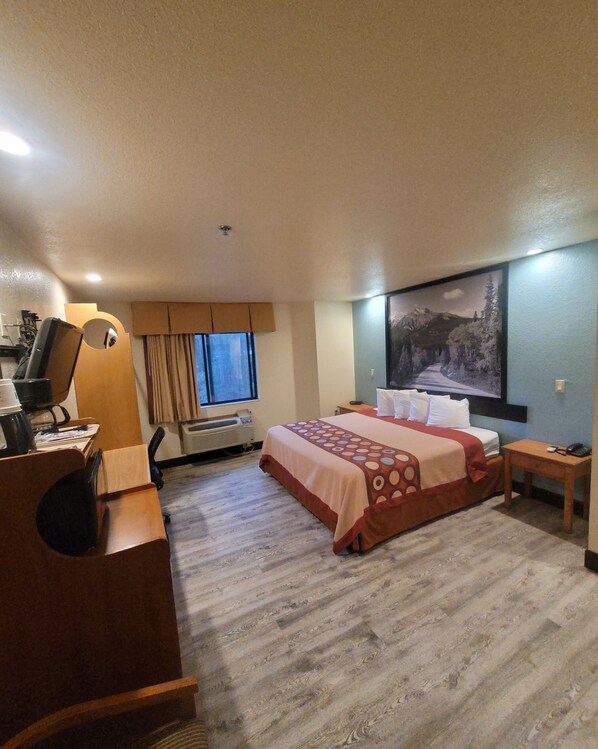 A hotel room with a bed, a desk with a chair, a window with curtains, an air conditioning unit, and a painting on the wall. - Super 8 by Wyndham Show Low (Show Low)