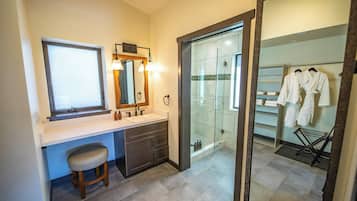 Une salle de bain équipée d’un meuble-lavabo, d’un miroir, d’une douche et d’un porte-serviettes avec des peignoirs.