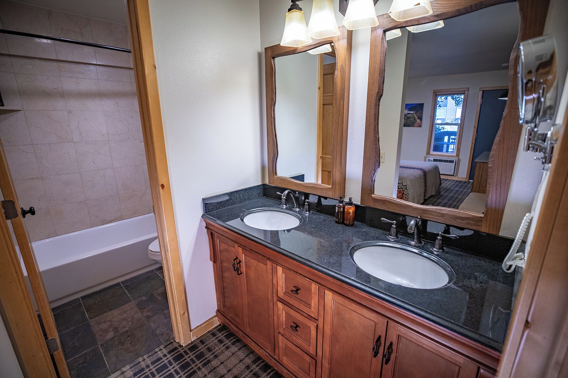 A bathroom with two sinks, wooden cabinets, a large mirror, and a bathtub.