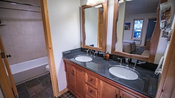 A bathroom with two sinks, wooden cabinets, a large mirror, and a bathtub.