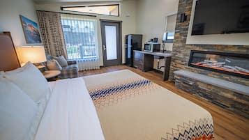A hotel room with a bed, a desk, a TV, a fireplace, and a balcony with curtains.
