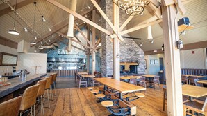 A spacious restaurant with high ceilings, exposed beams, and a stone wall. Tables and chairs are arranged for dining. - Outbound Mammoth  (Mammoth Lakes)