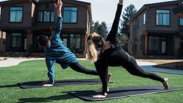 Dos personas practicando yoga sobre esterillas al aire libre frente a una casa moderna con un césped cuidado.