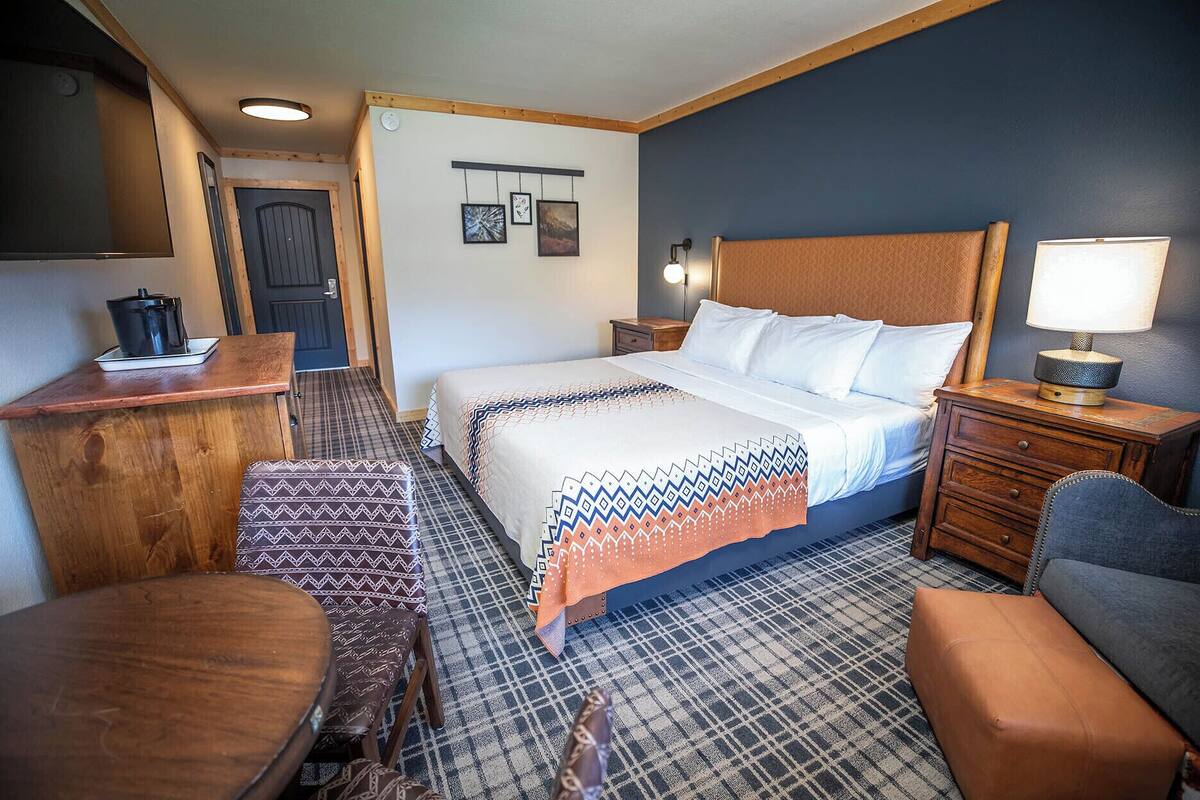 A hotel room with a bed, a desk, a chair, a nightstand, and a lamp.