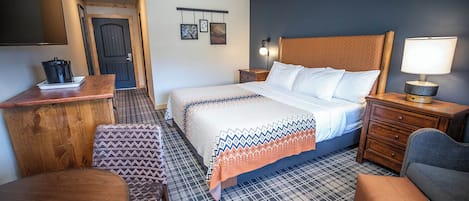 A hotel room with a bed, a desk, a chair, a nightstand, and a lamp.
