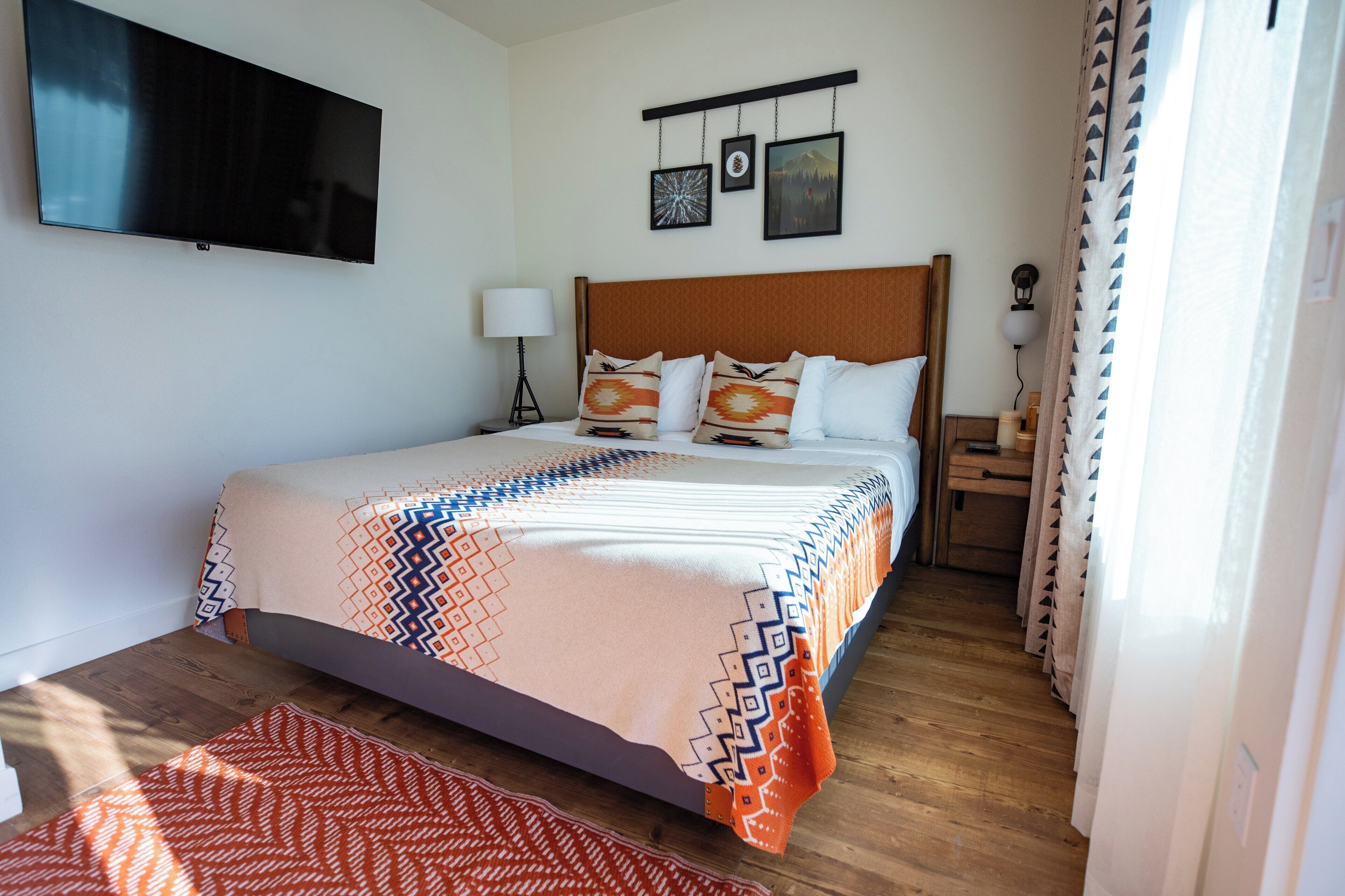 Camera d'albergo con un letto, una TV a schermo piatto, un comodino, una lampada e un quadro appeso al muro.