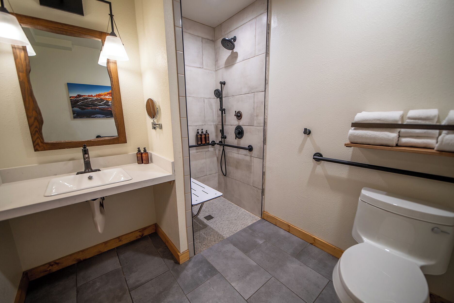 Et moderne badeværelse med hvid vask, spejl og toilet. Der er en bruser med håndbruser og et håndklædetørrestativ.