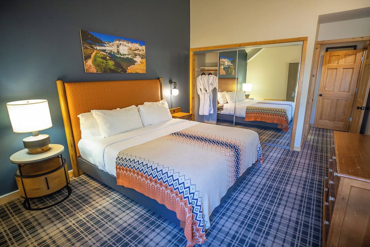 A hotel room with a large bed, a bedside table with a lamp, a mirror, and a painting on the wall.