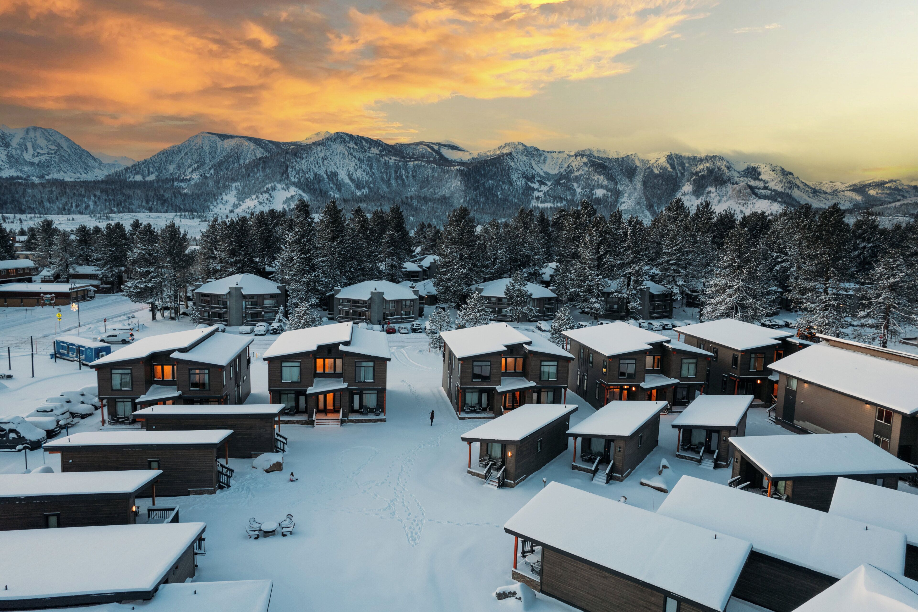 Ein verschneiter Wohnbereich mit modernen Häusern, wolkenlosem Himmel und Bergen im Hintergrund.