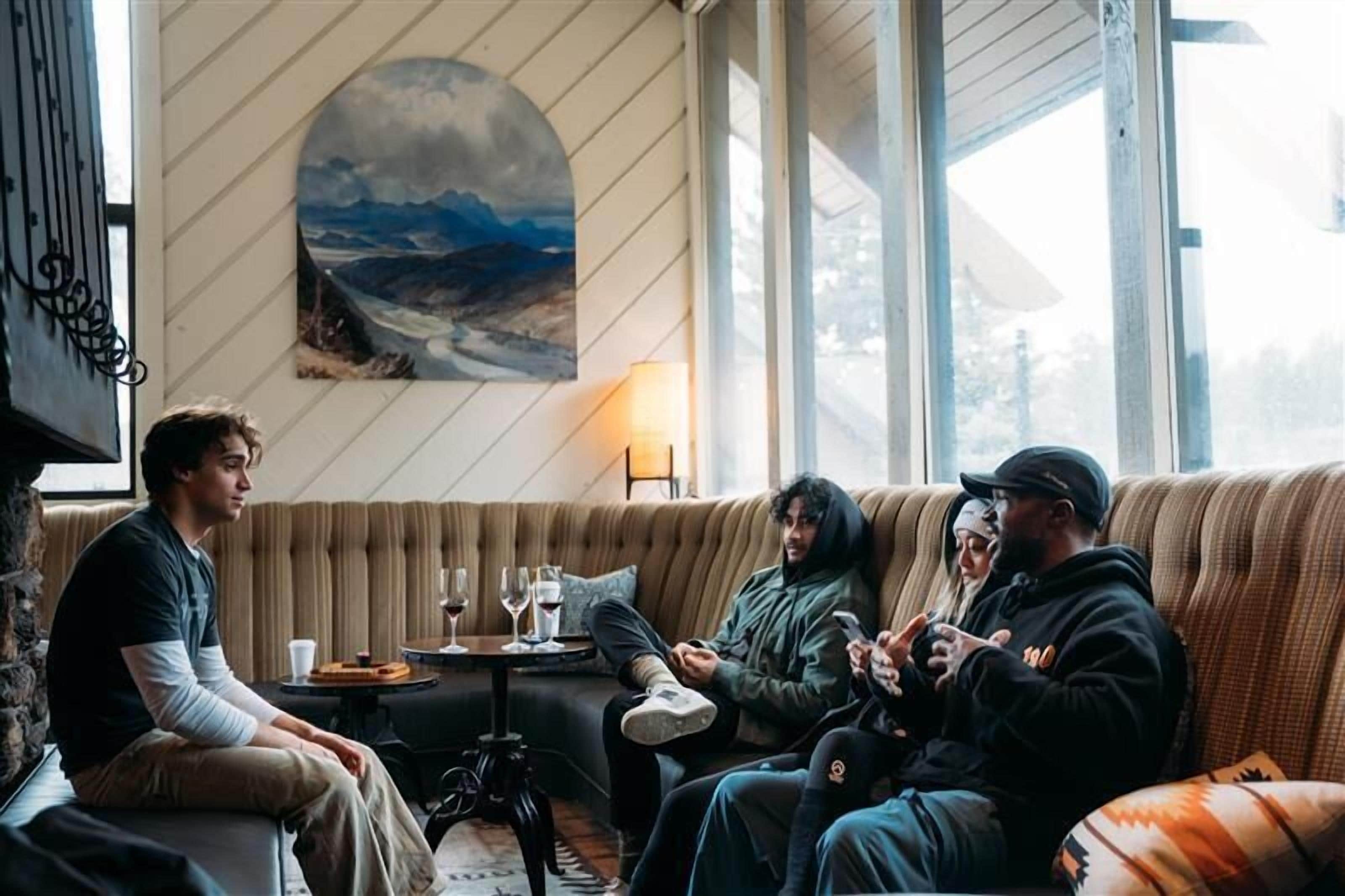 Et værelse med et stort vindue, et landskabsmaleri og et bord med glas og en tallerken.