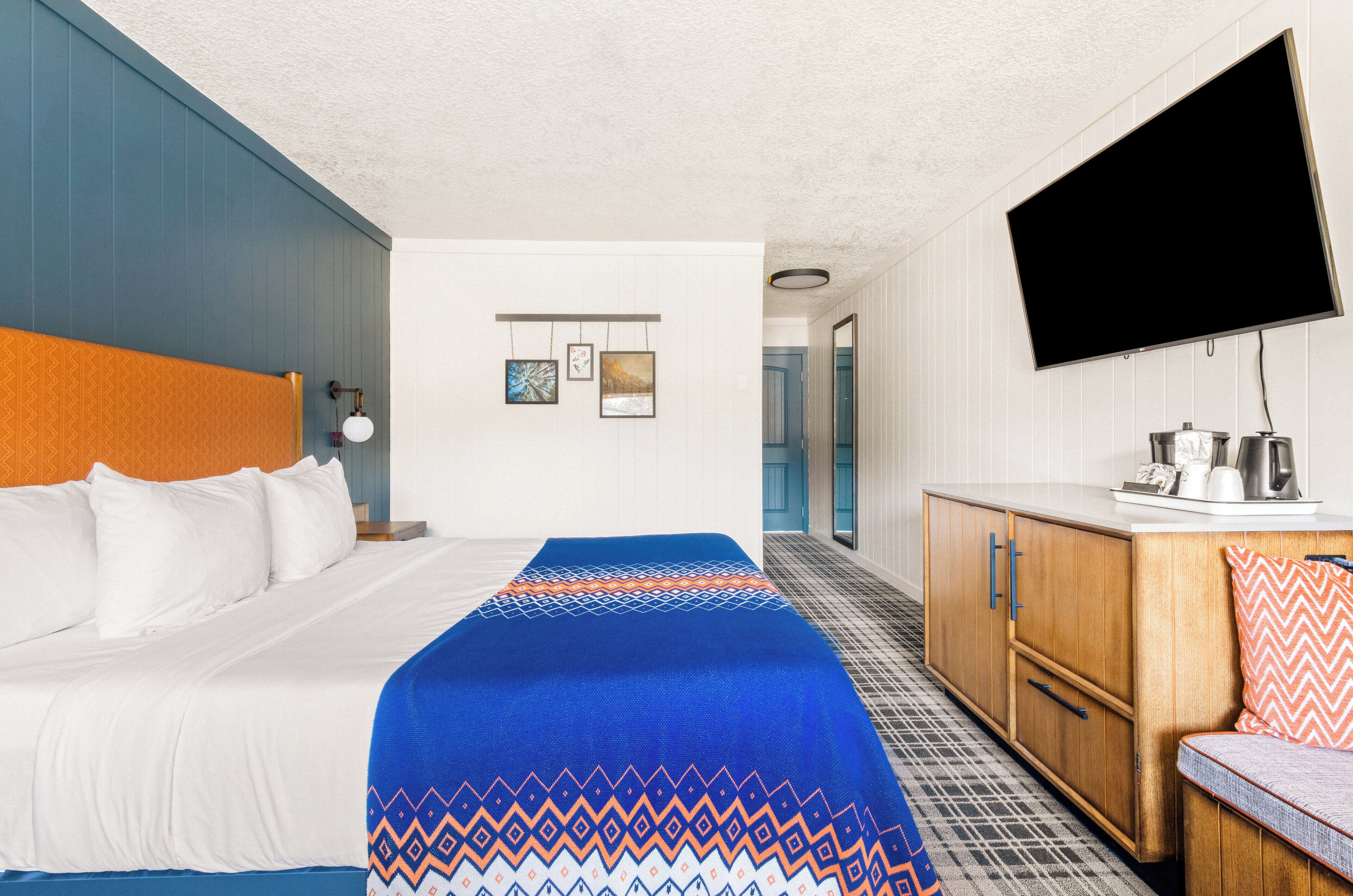 Una habitación de hotel con una cama, un escritorio, un televisor y una puerta que da a otra habitación.