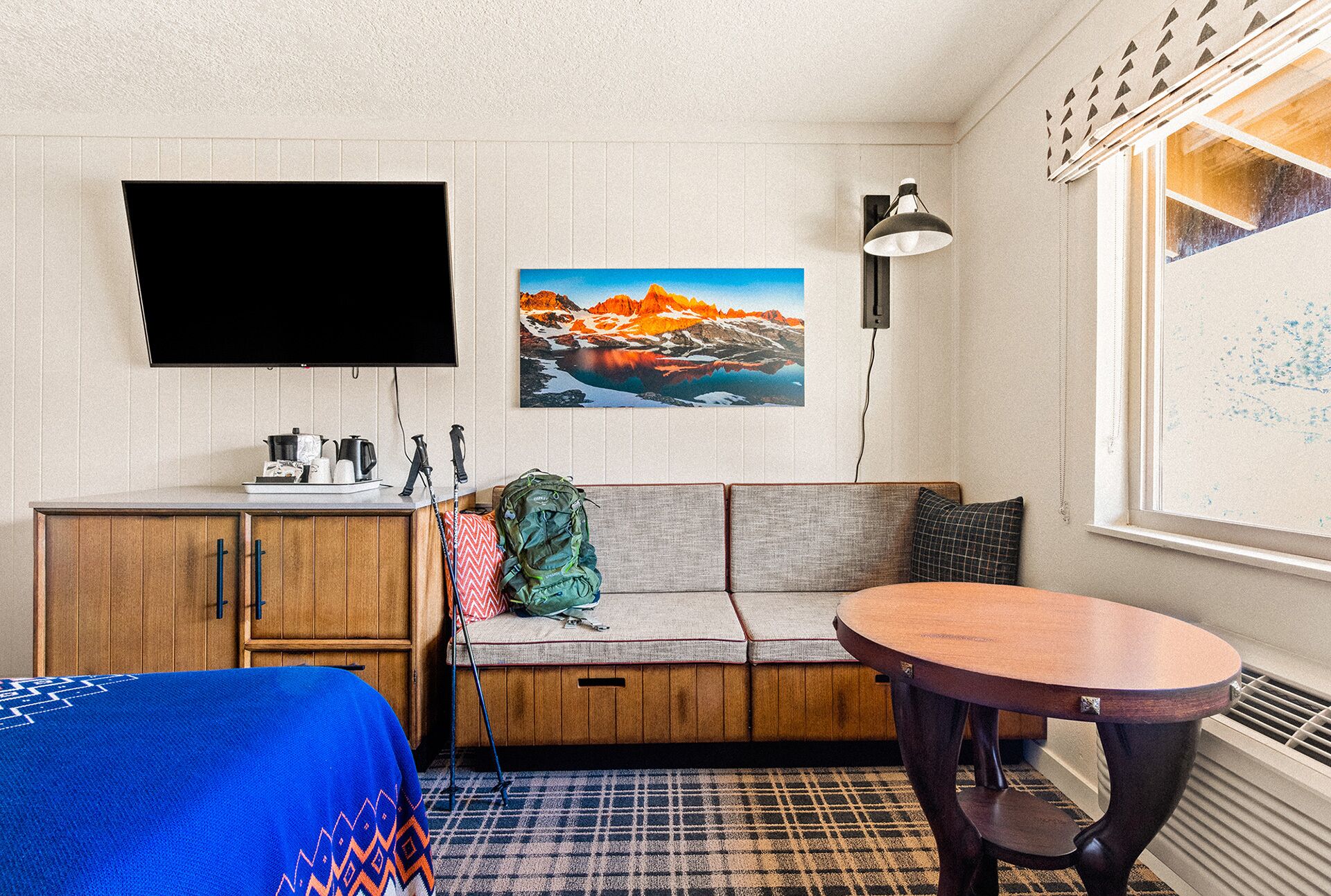 Una habitación compacta con un armario de madera, un sofá, una pequeña mesa redonda y un televisor instalado en la pared.