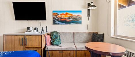 Una habitación compacta con un armario de madera, un sofá, una pequeña mesa redonda y un televisor instalado en la pared.