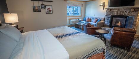A hotel room with a large bed, a fireplace, a sofa, and a television.
