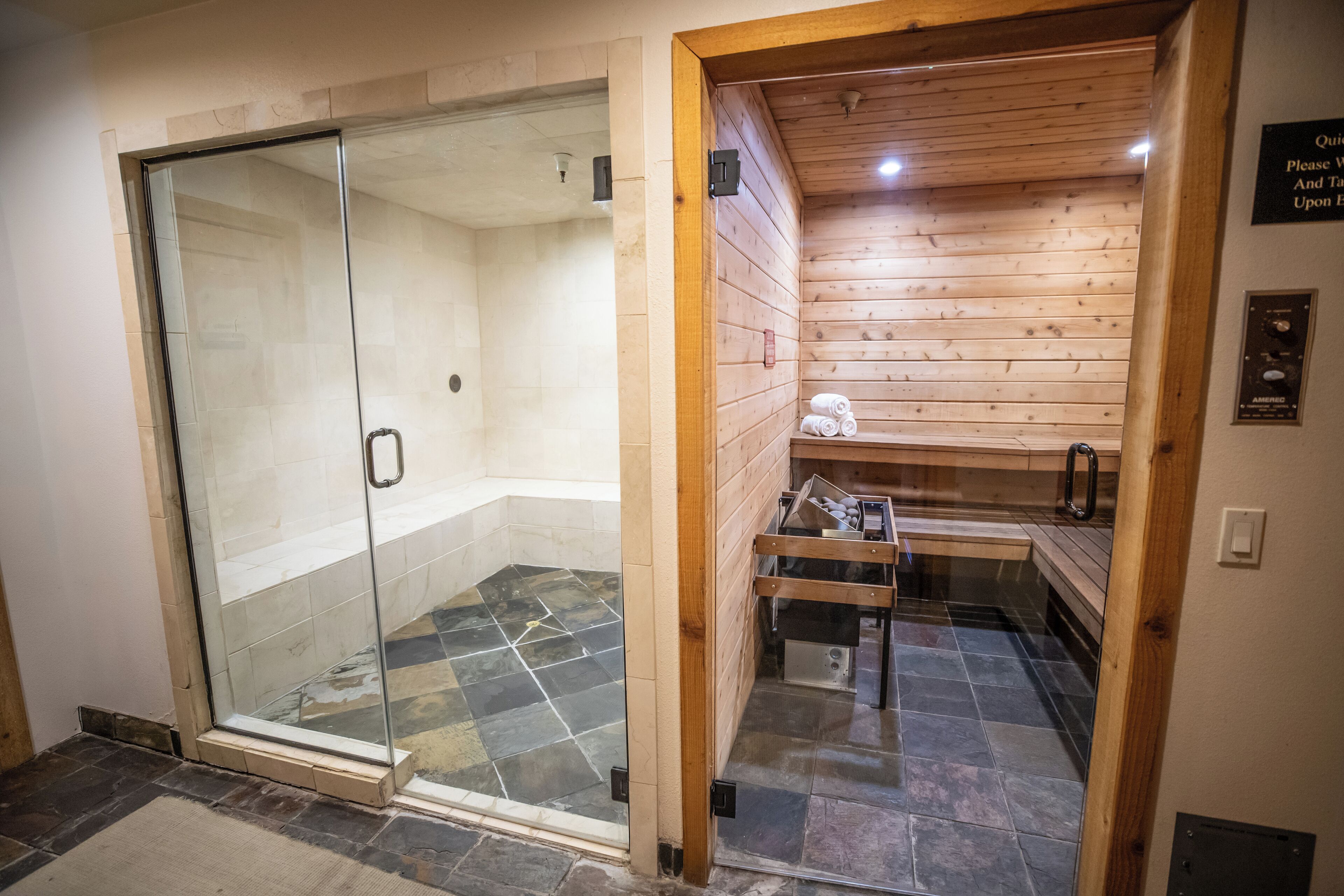 A sauna with a glass door, wooden walls, and a tiled floor.