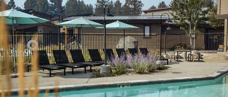 A swimming pool with lounge chairs and umbrellas, surrounded by a fence and vegetation.