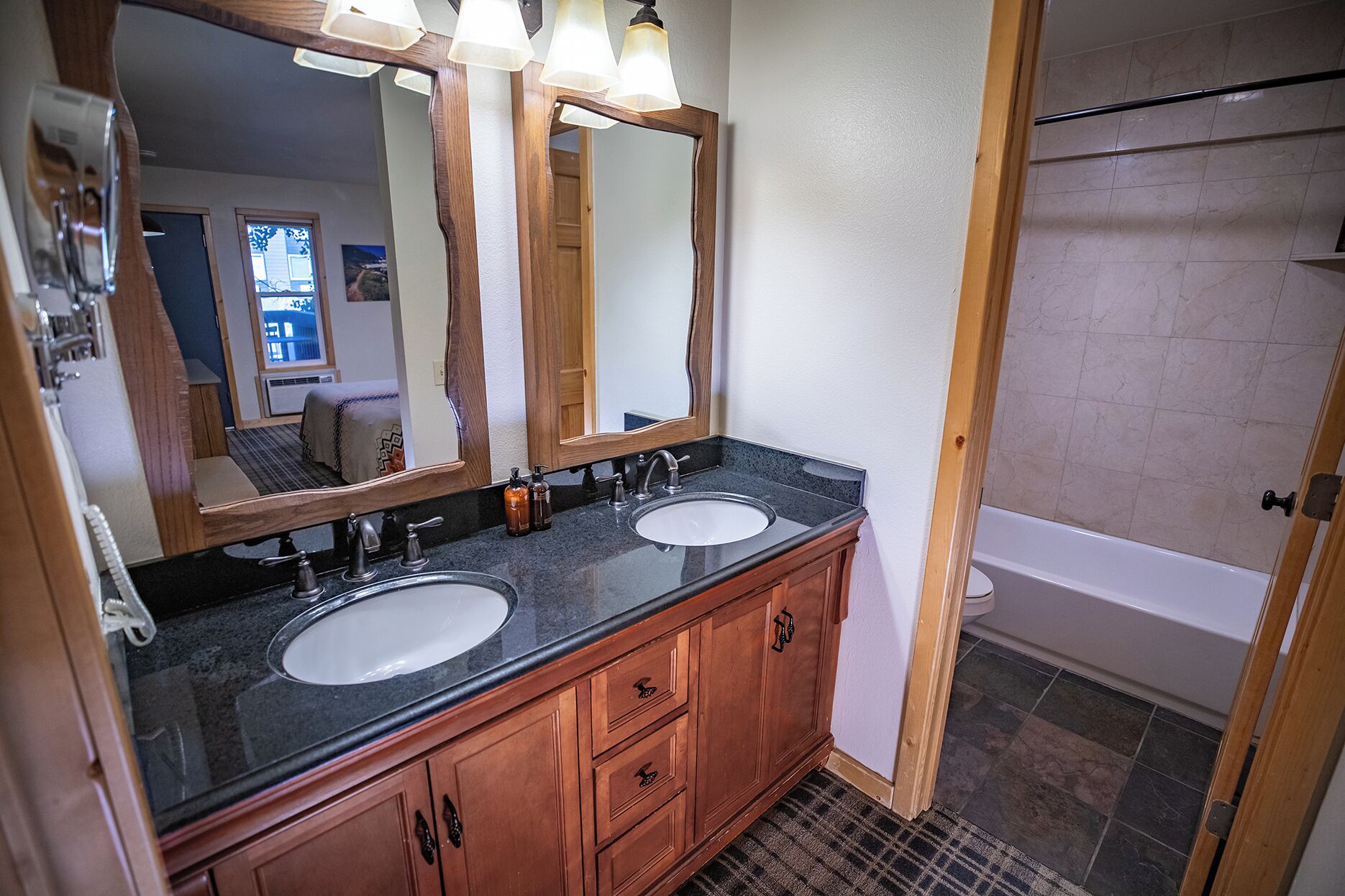 A bathroom with two sinks, wooden cabinets, a large mirror, and a shower area.