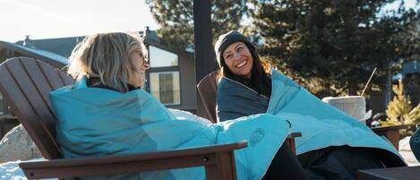 Two people sitting on a wooden deck chair outdoors with a house and trees in the background.