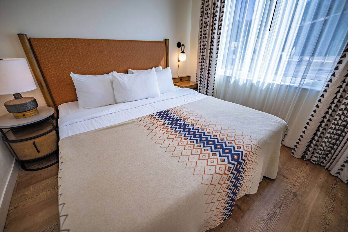 A hotel room with a bed, a nightstand, a lamp, and curtains.