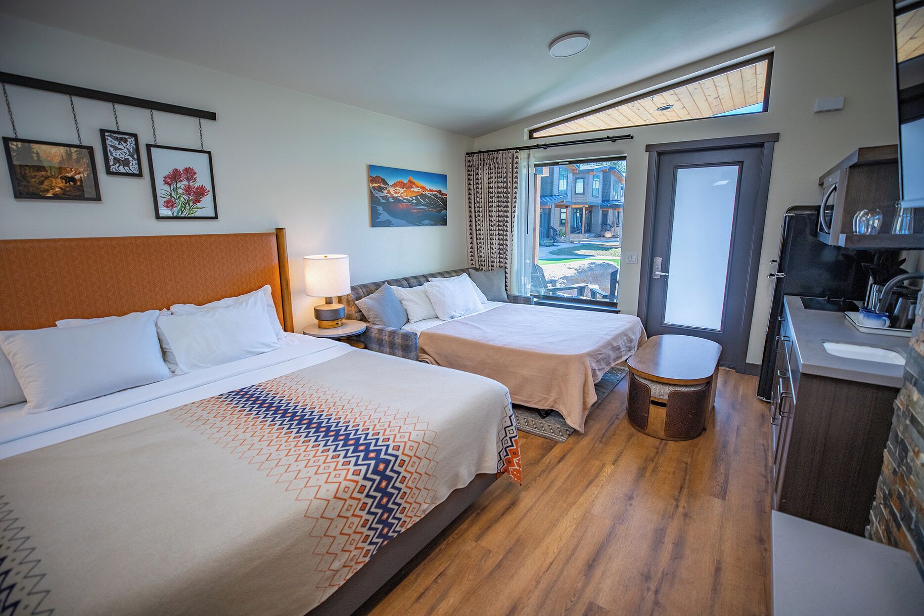 Une chambre d’hôtel avec deux lits, un coin repas et une vue sur un immeuble, visible à travers une porte vitrée.