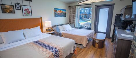 A hotel room with two beds, a dining area, and a view of a building through a glass door.