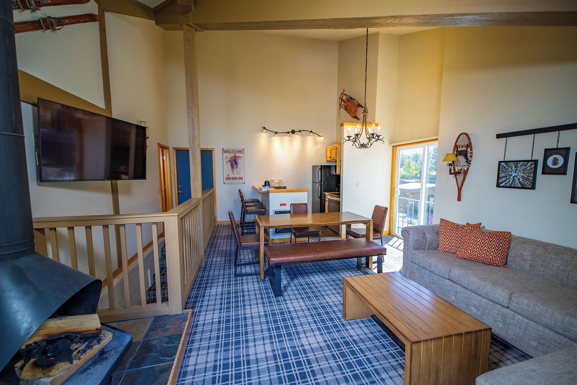 Een gezellige woonkamer met een bank, salontafel en een aan de muur bevestigde televisie. Er is een eethoek met een tafel en stoelen, en een keuken op de achtergrond.