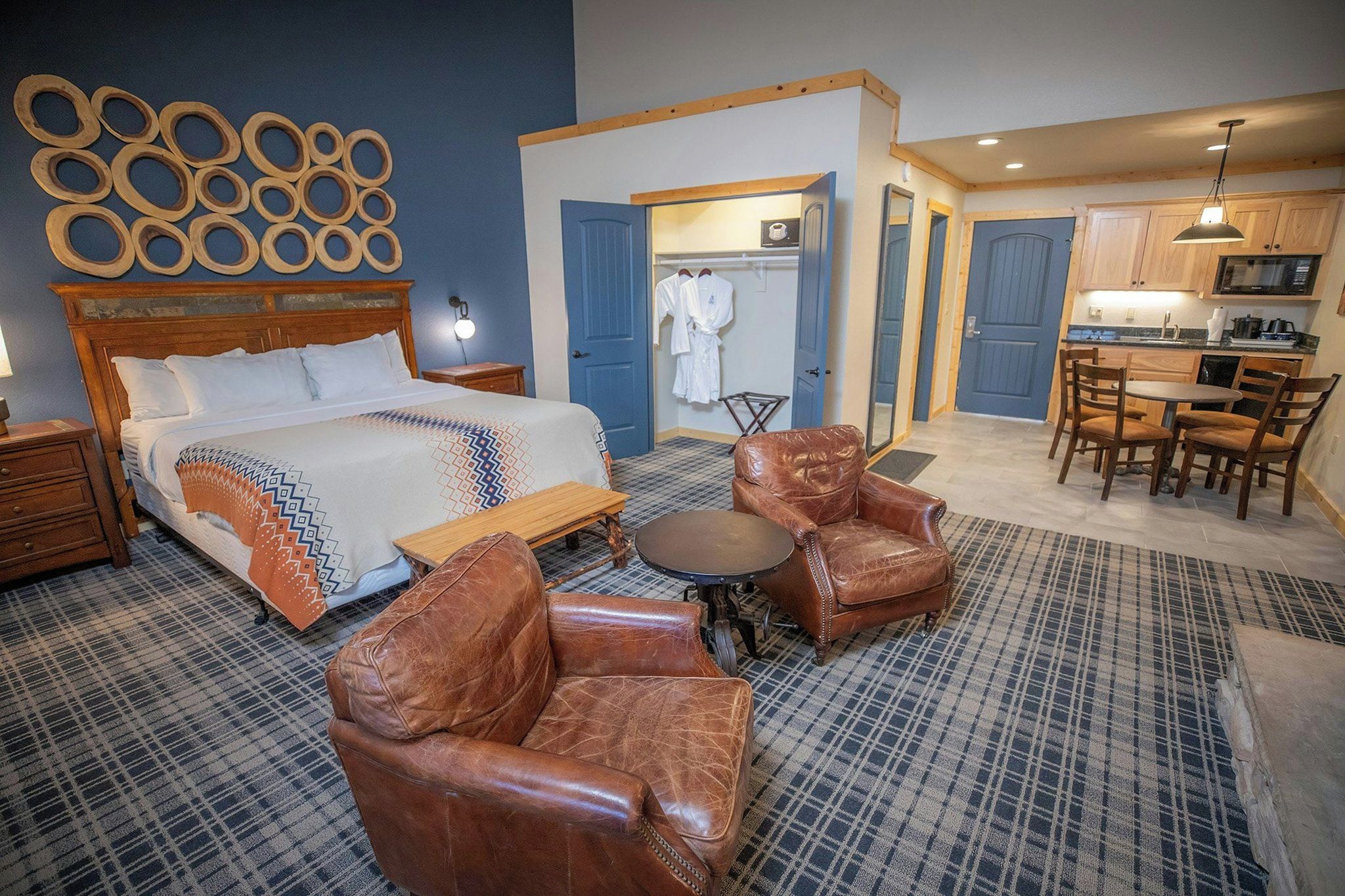 A hotel room with a bed, two leather armchairs, a small round table, and a bathroom visible through an open door.