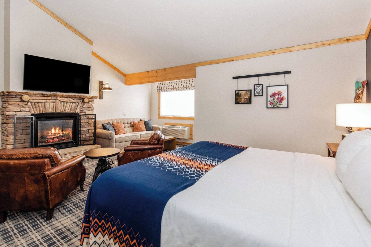 A hotel room with a stone fireplace, a large bed, a sofa, and a television mounted on the wall.