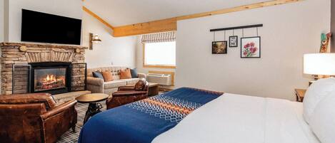 A hotel room with a stone fireplace, a large bed, a sofa, and a television mounted on the wall.
