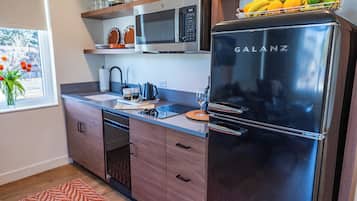 A modern kitchen with a stainless steel refrigerator, microwave, and dishwasher. There are wooden cabinets and a window with a view.
