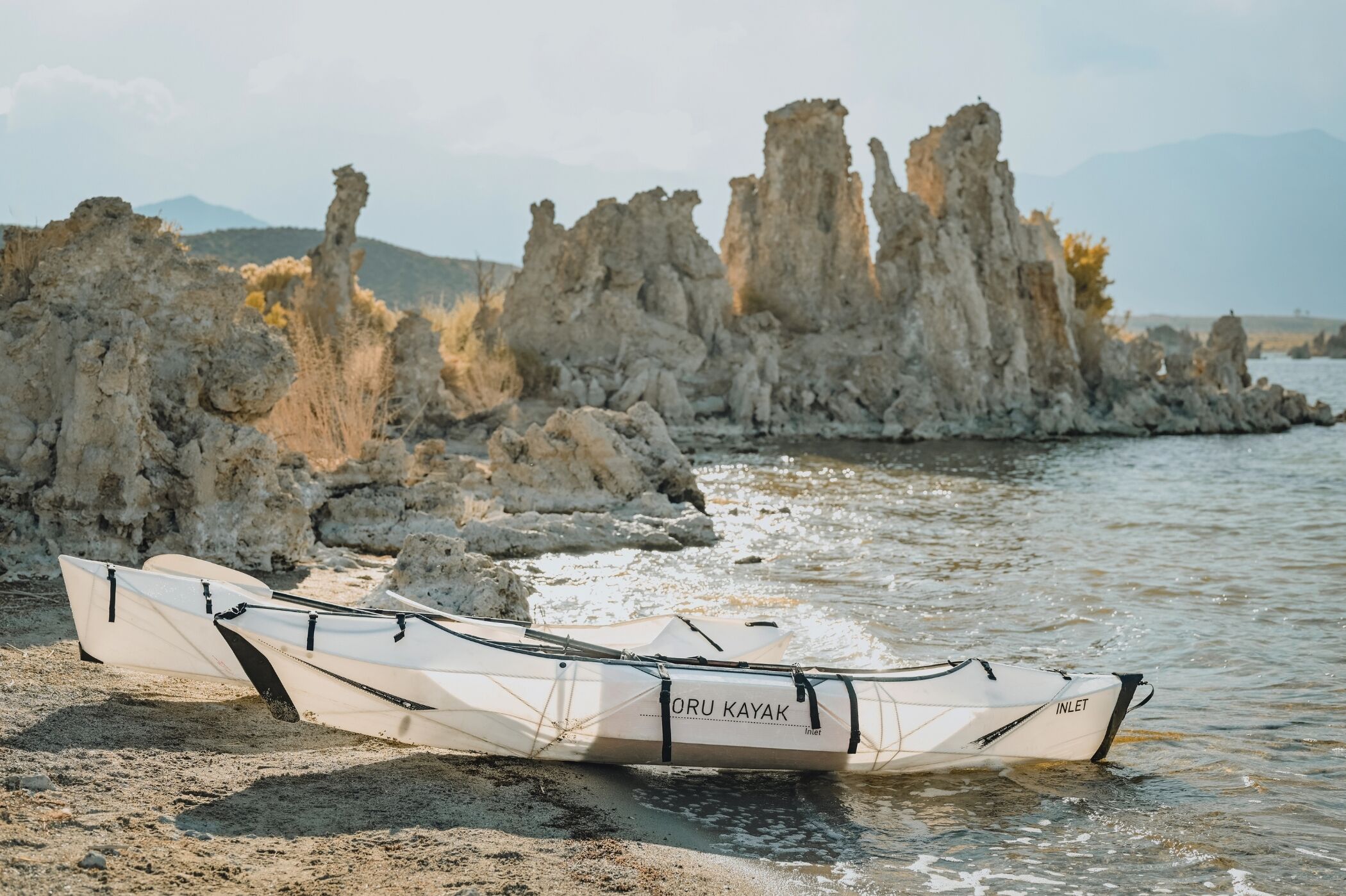 Ein Kajak namens "ORU KAYAK" am sandigen Ufer, im Hintergrund Felsformationen.