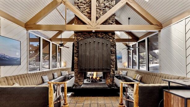 A cozy living room with a stone fireplace, wooden beams, and a large window overlooking a snowy landscape. - Outbound Mammoth  (Mammoth Lakes)
